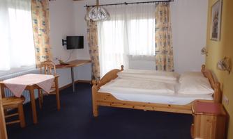 A cozy room with a double bed and a table. Large windows let in plenty of light and create a friendly atmosphere.