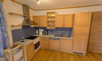 A modern kitchen with wooden cabinets and blue tiles. It includes cooking appliances, a sink, and a dining table.