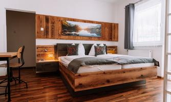 A modern bedroom with wood decor and a large bed. The room is bright and welcoming, with a table and chairs as well as a window for plenty of daylight.