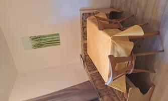 A small dining area with a round table and chairs. On the wall hangs a picture of green plants.