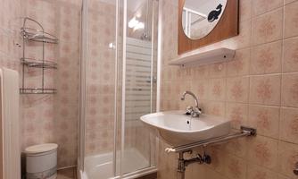 A small bathroom with a shower and a sink. The walls are decorated with pale tiles.