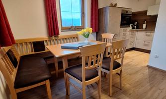 A cozy kitchen with a wooden dining area, a table, and four chairs. The window offers light and a view, and there are fresh flowers on the table.