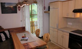 A modern kitchen with a wooden table and chairs. The room is bright and welcoming, with a window view to the outdoors.