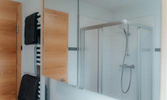 A modern bathroom with a glass shower cabin. Fresh towels hang on the wall, and wooden details add a warm touch.