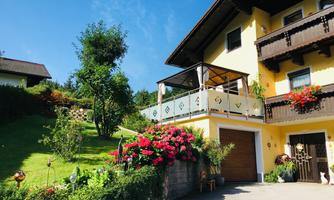 A beautiful house with a terrace and blooming flowers. The green surroundings and clear sky create an inviting atmosphere.