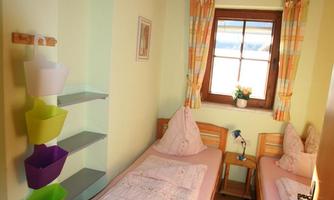 A cozy room with two single beds and bright walls. There is a window with a view outside and a decorative wall shelf.
