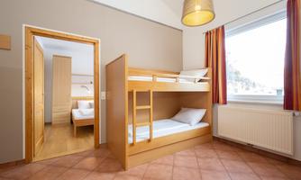 A bright room with a bunk bed in warm wooden tones. Light is shining through the window, and the space feels inviting.