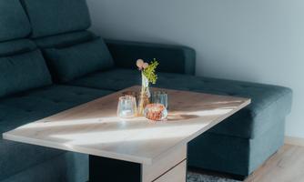 A cozy living area with a dark couch and a wooden coffee table. On the table are vases with flowers and glasses.