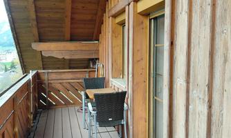 A wooden balcony with a table and two chairs. The wooden cladding and the view create a cozy atmosphere.