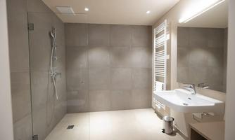 A modern bathroom with a large shower and an elegant sink. The walls are tiled with gray tiles and the lighting is bright.