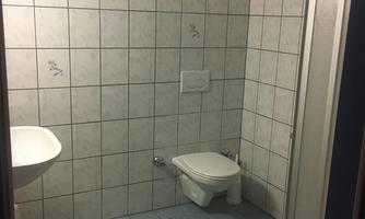 A small, simple bathroom with tiled walls. It contains a shower, a sink, and a toilet.