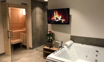 A modern bathroom with a whirlpool and a sauna. A television showing a fireplace hangs on the wall.