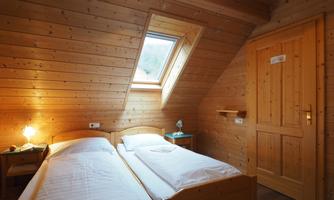 A cozy room with wooden walls and two single beds. A window provides daylight and a warm atmosphere.