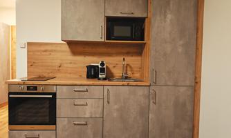 A modern kitchen with gray surfaces and wooden details. It is equipped with a stove, a microwave, and a kettle.