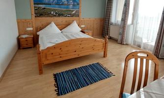 A cozy bedroom with a wooden bed and two pillows. A large picture of a landscape hangs on the wall, and the room has plenty of natural light.