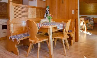 A cozy dining area made of wood with a round table and two benches. A vase with fresh tulips sits on the table.