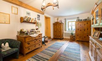 A cozy room with wooden furniture and a colorful rug. Bookshelves and decorations hang on the wall.