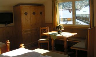 A cozy room with wooden furniture and a table. Sunlight is shining through the window and you can see snow outside.