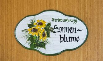 A decorative sign with the inscription "Holiday Apartment Sunflower". It features yellow sunflowers and is placed on a wooden background.