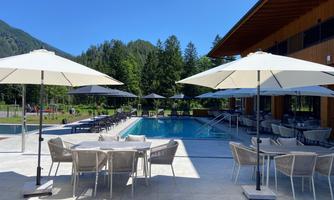 A modern pool area with sun umbrellas and comfortable seating. In the background, trees and mountains can be seen.