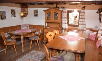 A cozy dining room with wooden furniture and traditional decor. The tables are covered with checkered tablecloths and there are also some pictures on the wall.