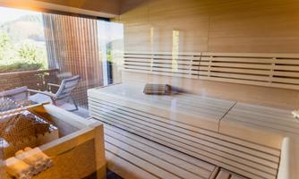 A modern sauna area with bright wooden interiors and a large window front. In the background, a terrace with outdoor furnishings is visible.