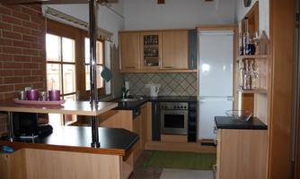 A modern kitchen with wooden cabinets and a refrigerator. The windows let in plenty of light and create an inviting atmosphere.