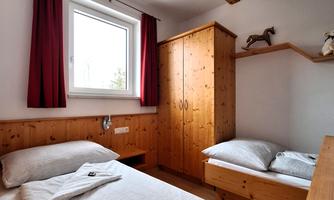 A cozy bedroom with two single beds and a wooden wardrobe. The walls are light, and a window provides daylight.