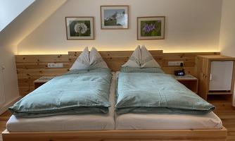 A cozy bedroom with a large double bed and light wooden furniture. Some pictures are hanging on the walls and the lighting creates a pleasant atmosphere.