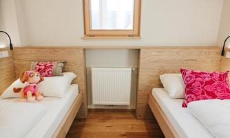 A cozy room with two beds and colorful cushions. On the bed lies a small plush dog.