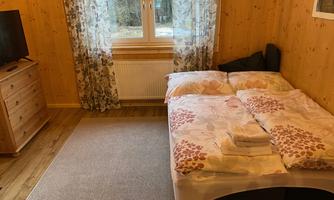 A cozy bedroom with a double bed and a large window. The walls are made of wood, and there is a television as well as a dresser.