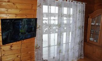 A cozy room with wood paneling, a television on the wall, and a window with curtains. Decorative elements and a view outside can be seen in the background.