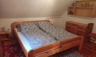 A cozy bedroom with a large wooden bed and blue blankets. Next to the bed, there is a shelf and a wooden dresser.