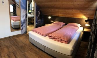A cozy bedroom with two beds and a wooden ceiling. The room is bright and inviting, with a mirror and soft colors.