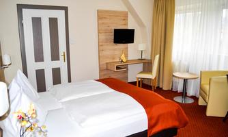 A cozy hotel room with two beds and modern furniture. There is a window with curtains, a small table, and a TV on the wall.