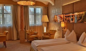 An elegant hotel room with a large bed and comfortable armchairs.  
Plenty of daylight comes through the windows, creating an inviting atmosphere.