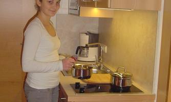 A young woman is cooking in a modern kitchen. She is holding a pot in her hand and smiling.