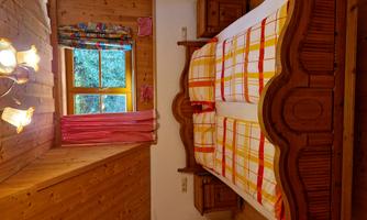 A cozy bedroom with a large wooden bed and checkered blankets. The walls are adorned with wood paneling, and a window lets in plenty of daylight.