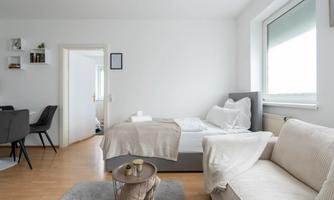 A modern room with a bed, a couch, and a small table. The room has bright walls and plenty of natural light.