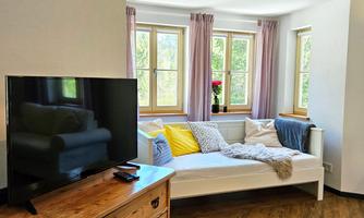 A cozy living room with a white daybed and colorful cushions. A wooden cabinet and a television complete the decor.
