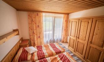 A cozy bedroom with two beds and wood paneling. Large windows bring plenty of daylight into the room.