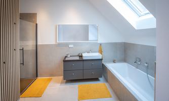 A modern bathroom with a shower, a bathtub, and a large window. The decor is bright and elegant, with yellow bath mats.