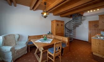 A cozy living space with wooden details and a charming dining area. A spiral staircase leads upstairs, the atmosphere is inviting and warm.