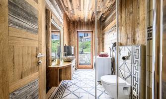 A modern bathroom with wood paneling and stylish tiles. It has a large window that lets in daylight and an elegant shower.