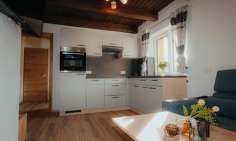A modern kitchen with a wooden ceiling and bright furniture. The room is well lit and comfortably furnished.