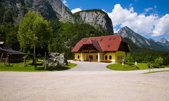 A charming building with a red roof in a picturesque landscape. In the background, tall mountains stand under a blue sky.