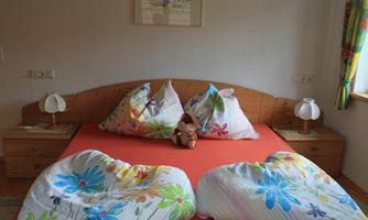 A cozy bedroom with a double bed and colorful bedspreads. A plush bear sits on the bed between two pillows.