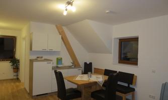 A modern and cozy kitchen with a dining table and chairs. The room has hardwood floors and large windows.