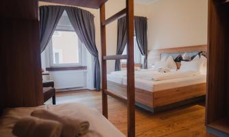 A cozy bedroom with two beds and soft bedding. Bright curtains let natural light in.
