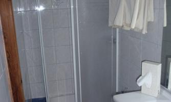A bathroom with a shower stall and a sink. Towels hang on the wall, and the floor is tiled with blue tiles.